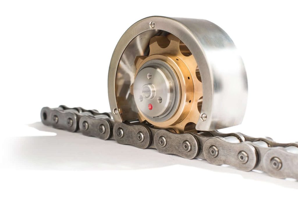 Sistema de lubricación de cadenas Rotalube PB fabricado en bronce fosforoso con cubierta metálica, engranado sobre una cadena de rodillos industrial.